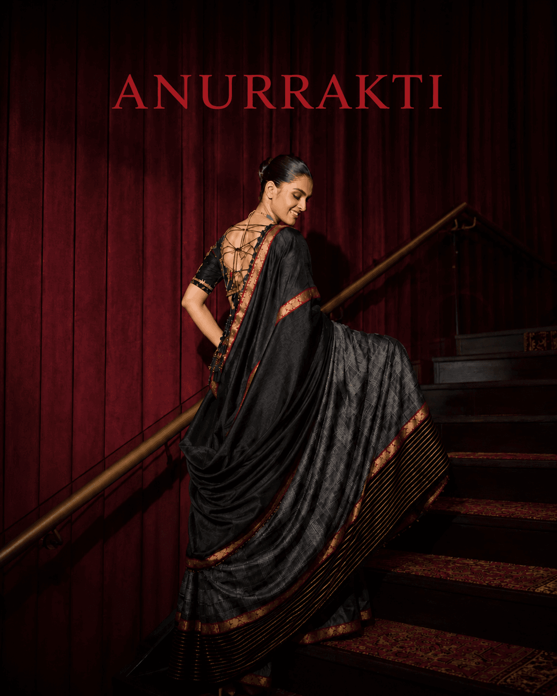 Model wearing a black and grey saree against a red velvet staircase